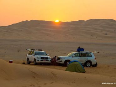 Two white SUVs and a tent in the desert at sunset.