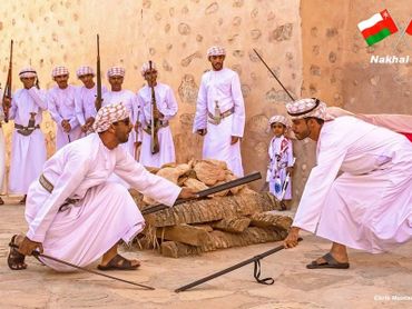 Traditional Omani men in white robes perform a cultural rifle dance at Nakhal Fort.