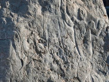 Ancient rock carving depicting human figures with raised arms.