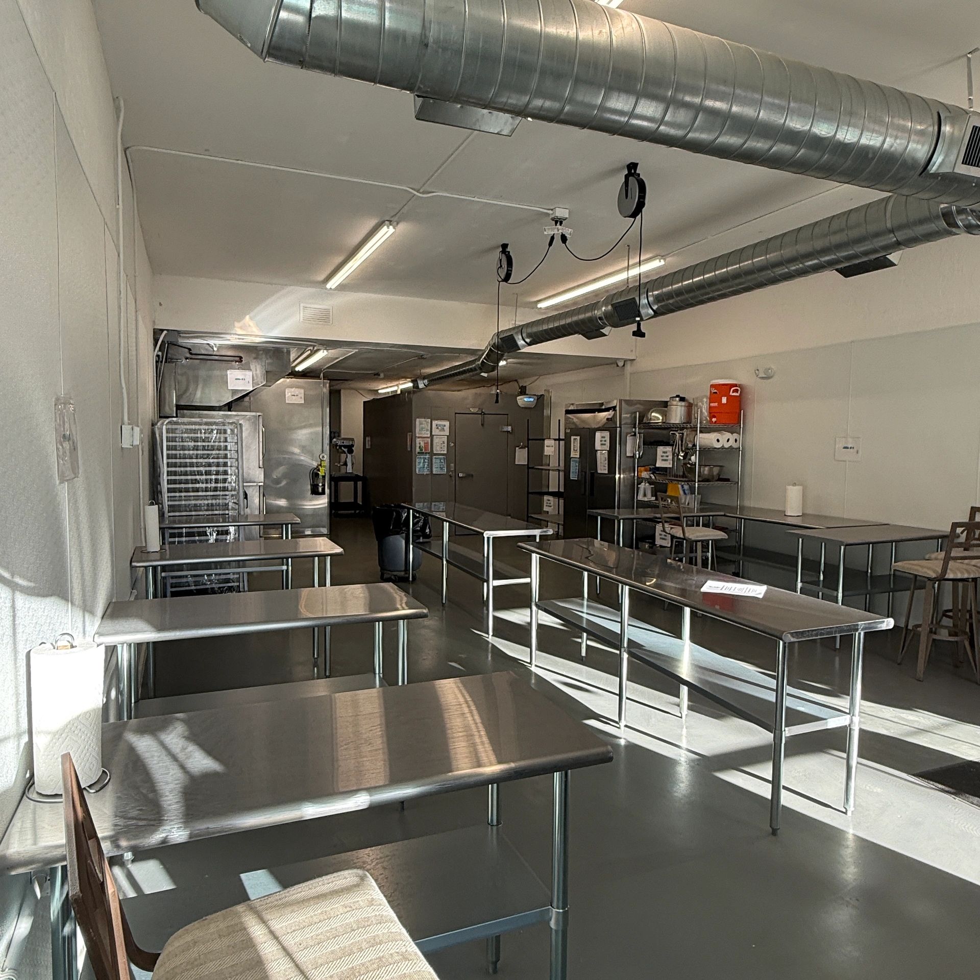 Industrial kitchen with stainless steel tables and ventilation ducts.