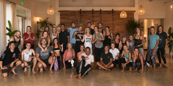 A large group of people posing together in a well-lit yoga studio.