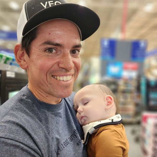 A smiling man holds a sleeping baby in a store setting.