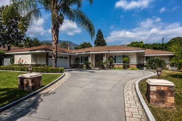 Single-story house with a curved driveway and lush landscaping.