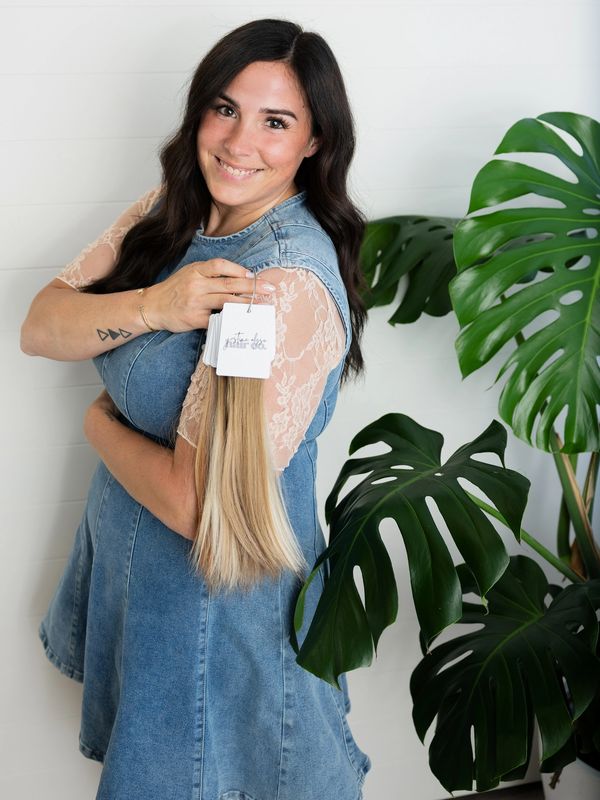 Smiling woman holding hair extensions with a plant nearby.