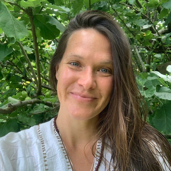 Smiling woman with long hair among green foliage.