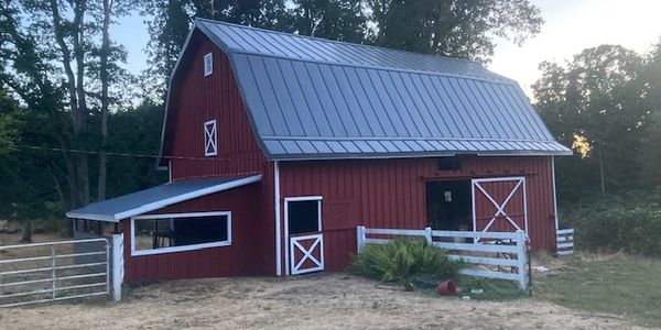 A red barn with white trim surrounded by trees at dusk.
