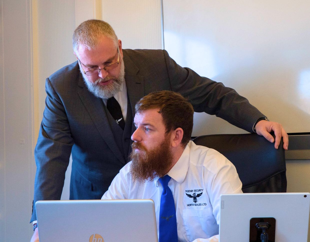 Two men in office attire working together at a desk with laptops.