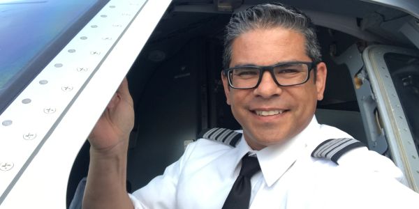 Smiling pilot in uniform at airplane cockpit door.