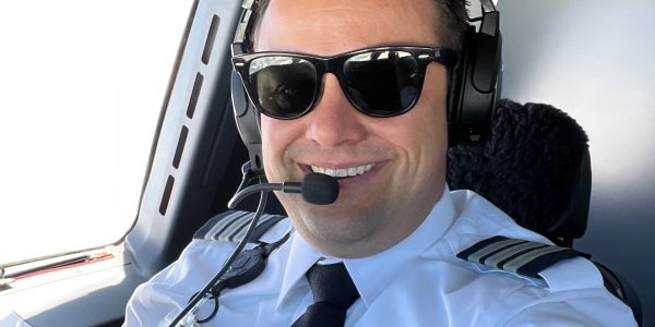 Smiling pilot wearing sunglasses and headset in airplane cockpit.