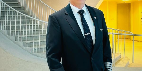 Pilot in uniform standing by a modern staircase indoors.