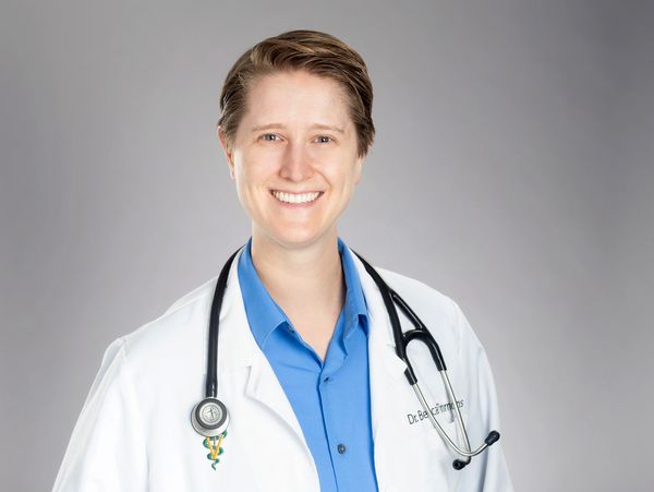 Smiling doctor in white coat with stethoscope on gray background.