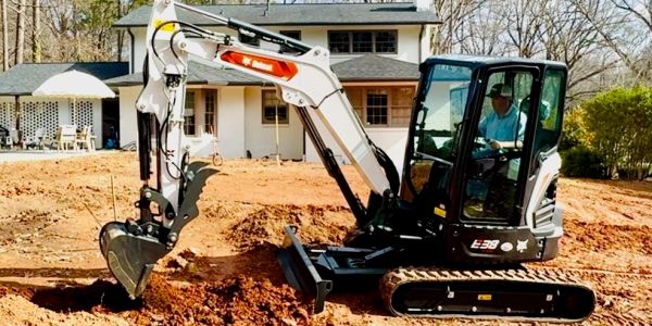 Mini excavator digging near a residential house.