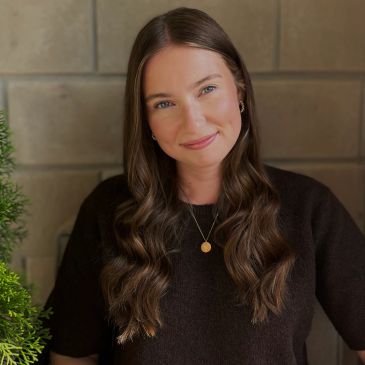 Smiling woman with long wavy hair wearing a black top and gold necklace.