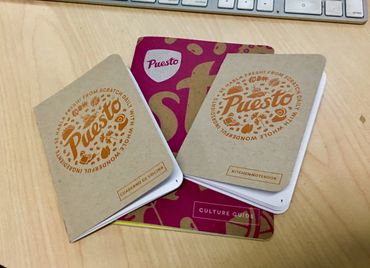 Two Puesto kitchen notebooks and a culture guide on a wooden desk.