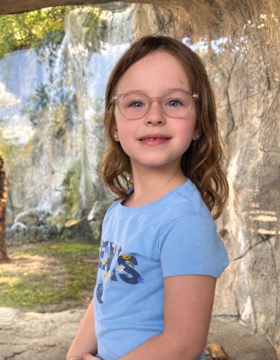Young girl smiling outdoors near a waterfall.