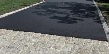 Newly paved asphalt driveway with a Belgium Block curb.