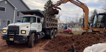 Excavator loading dirt into a dump truck at a residential construction site.