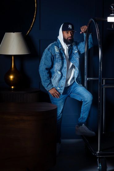 Man in denim jacket and white hoodie posing by luggage cart.NYC Headshot & Branding Photographer | Taisha Marie Photos