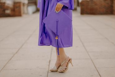 Person in purple graduation gown holding cap, wearing high heels. NYC Graduation & Prom Photographer | Taisha Marie Photos