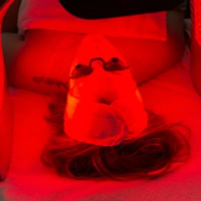 Client lying down receiving LED Light Therapy with a glowing red light mask over their face at Bloss