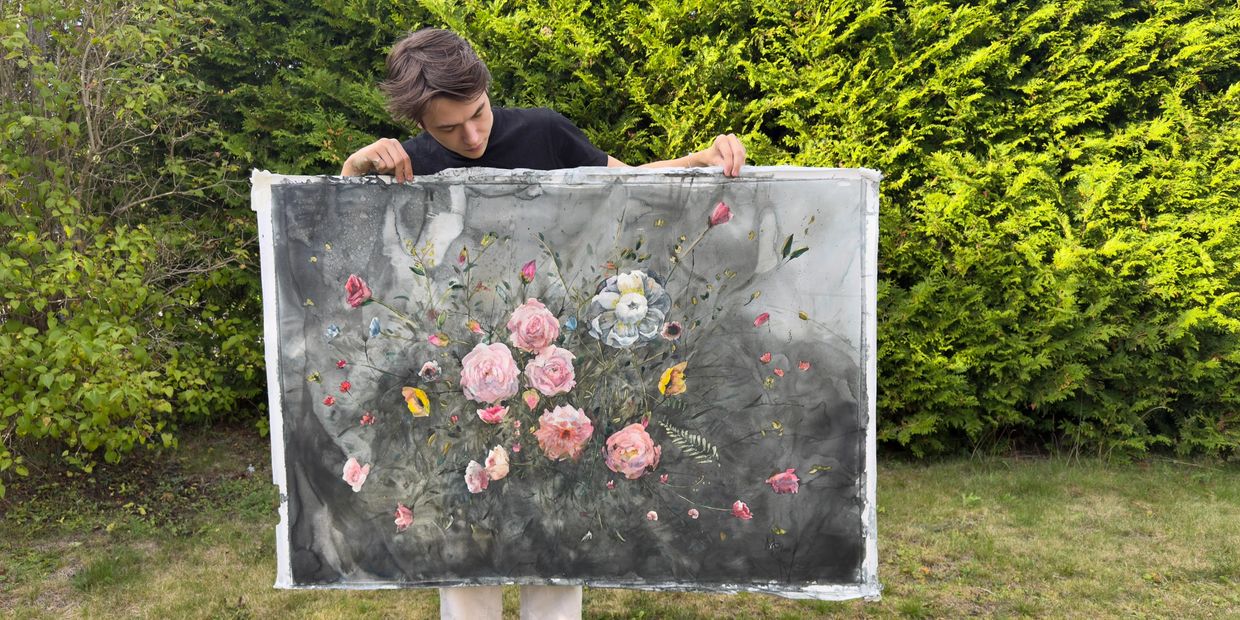 Person visar en målning med blommor utomhus.