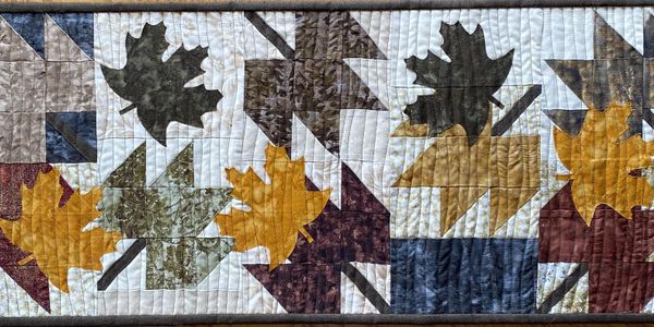 Quilted fabric with autumn leaf and geometric patterns in earth tones.