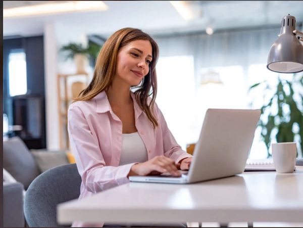 Woman smiling while using a laptop at a desk.