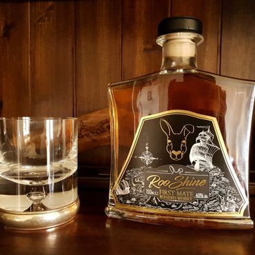 A bottle of Roo Shine whiskey and an empty glass on a wooden surface.