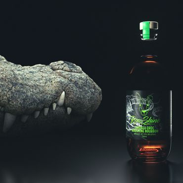 A crocodile's head next to a bottle of RooShine Smoked Croc Bourbon.