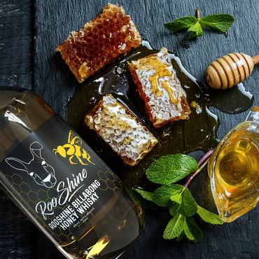Bottle of Rooshine honey whisky with honeycomb and fresh mint on a black slate.