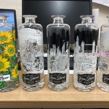 Five decorated glass bottles with intricate city maps and floral designs on a wooden surface.