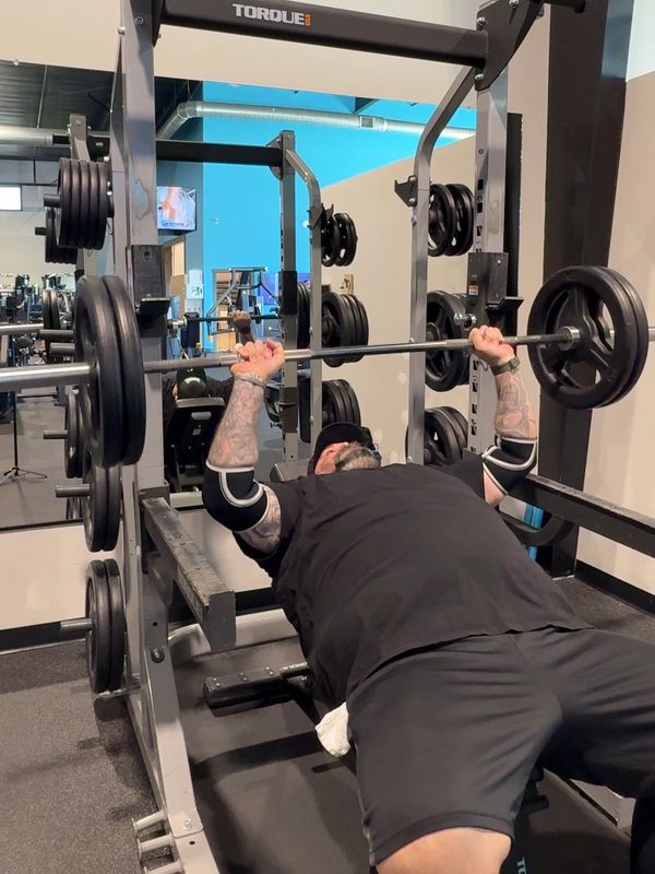 Man with tattoos bench pressing heavy weights in a gym.