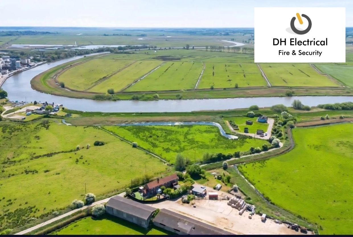 Aerial view of green farmland and a river with DH Electrical logo.