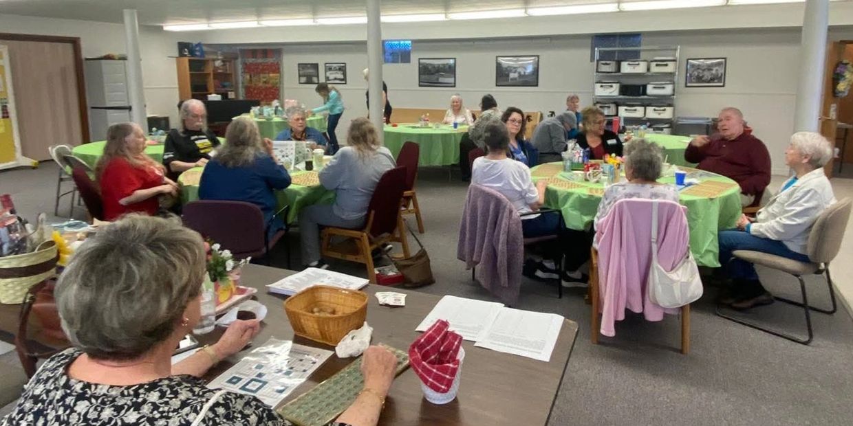 A group of elderly people gathered around tables playing bingo in a community center.