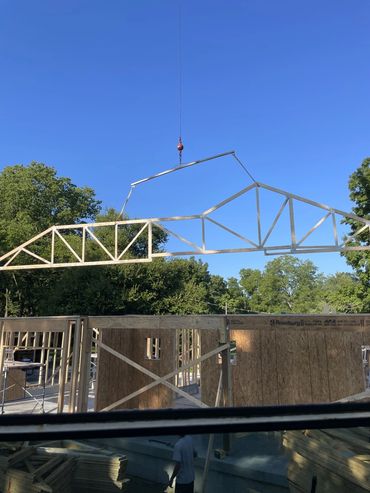 A crane lifts a large roof truss into position above a building under construction.