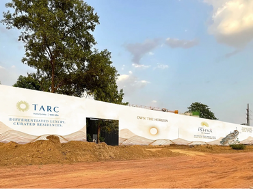 Construction site with a white promotional wall for TARC luxury residences under a clear sky.