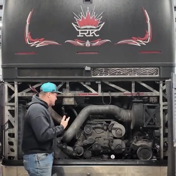 Man explaining a large truck engine inside an open engine compartment.
