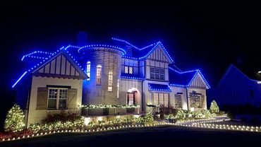 Large house decorated with blue and white Christmas lights at night.