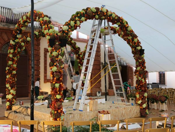 Floral arches being decorated indoors with workers on ladders.