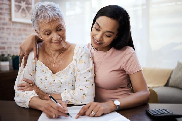 A caretaker helping an older woman sign a document