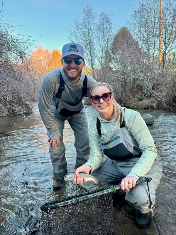 Two people in waders holding a fish in a river.