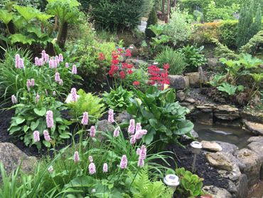 A lush garden with pink, red flowers and a small stone pond.