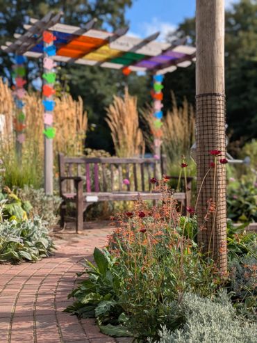 A colorful garden path with flowers, a wooden bench, and a pergola decorated with vibrant hanging ornaments.