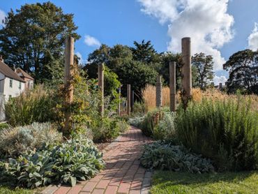 A peaceful garden path lined with lush plants and wooden posts under a blue sky.