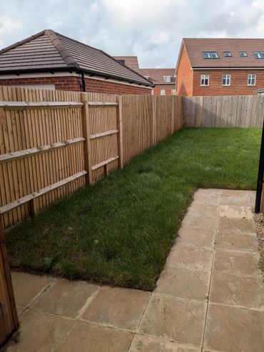 Backyard with green grass, stone tiles, and wooden fences around houses.