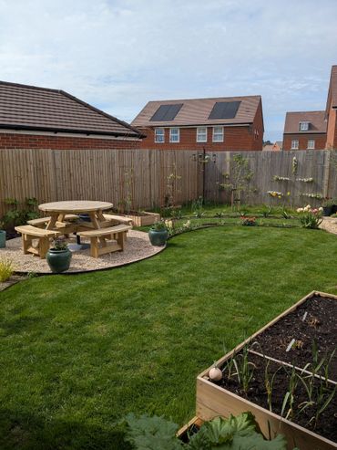 A well-maintained backyard with a wooden picnic table, raised garden bed, and flowering plants along the fence.