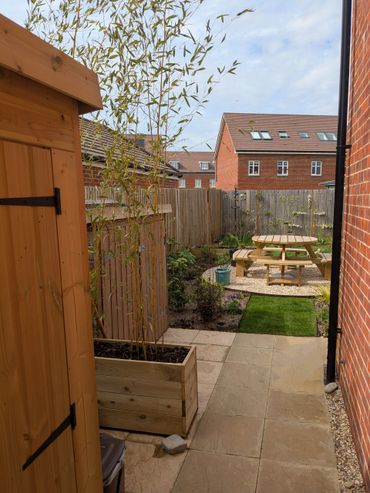 Cozy backyard with wooden shed, planter, and picnic table under a blue sky.