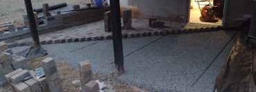 Under-construction brick patio with gravel foundation and construction tools.