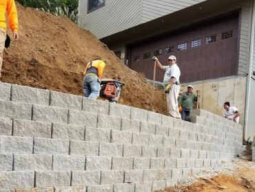Workers building a retaining wall outside a house.
