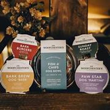 Variety of natural dog food packages from Raw Woofchester displayed on a wooden surface.